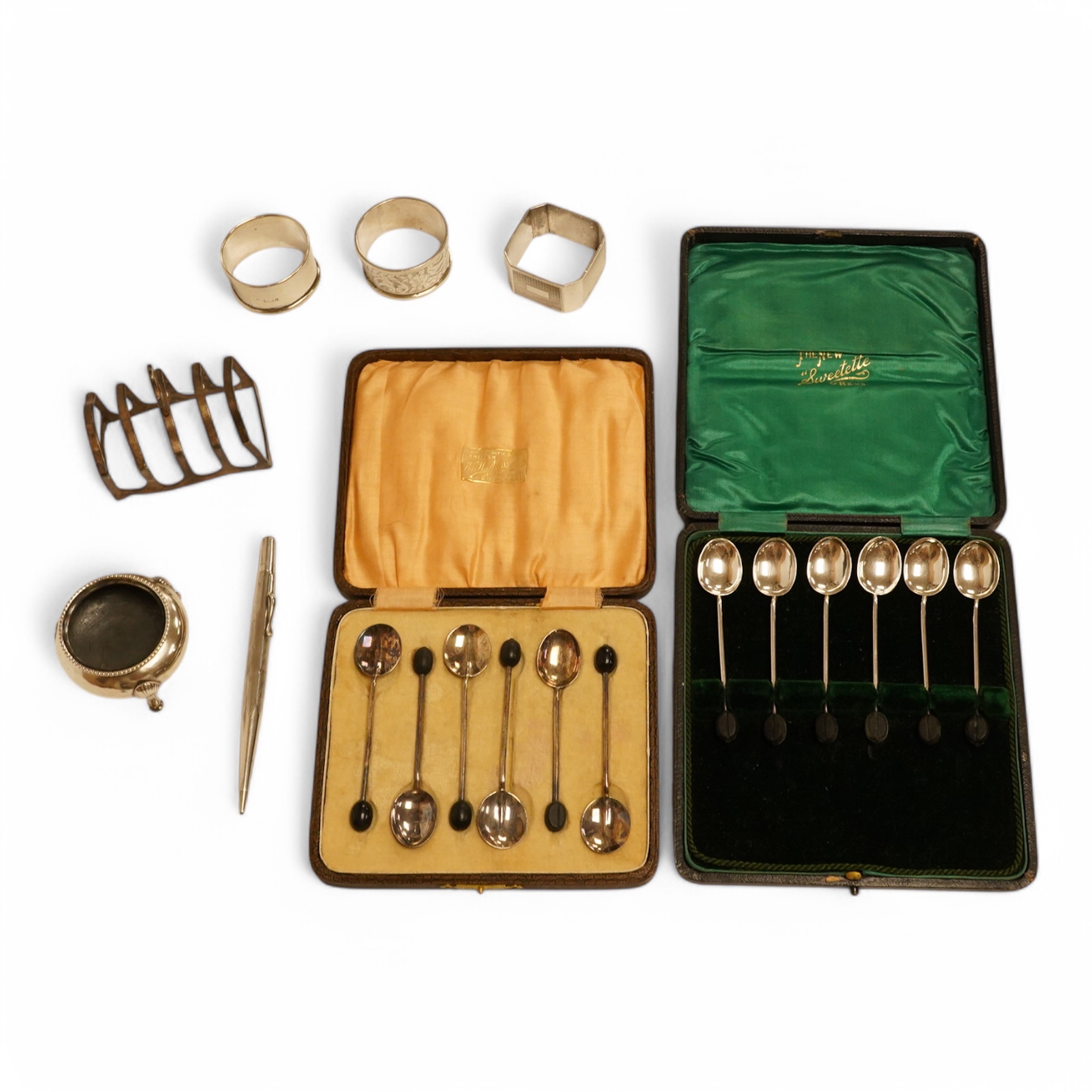 Two cased sets of six silver bean end coffee spoons, a Victorian silver bun salt, three assorted silver napkin rings, a small silver five bar toast rack and a sterling pen. Condition - poor to fair